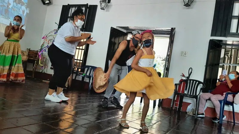 Una maestra guía a dos jóvenes con falda tradicional en el paso de los bailes cantaos durante un taller.