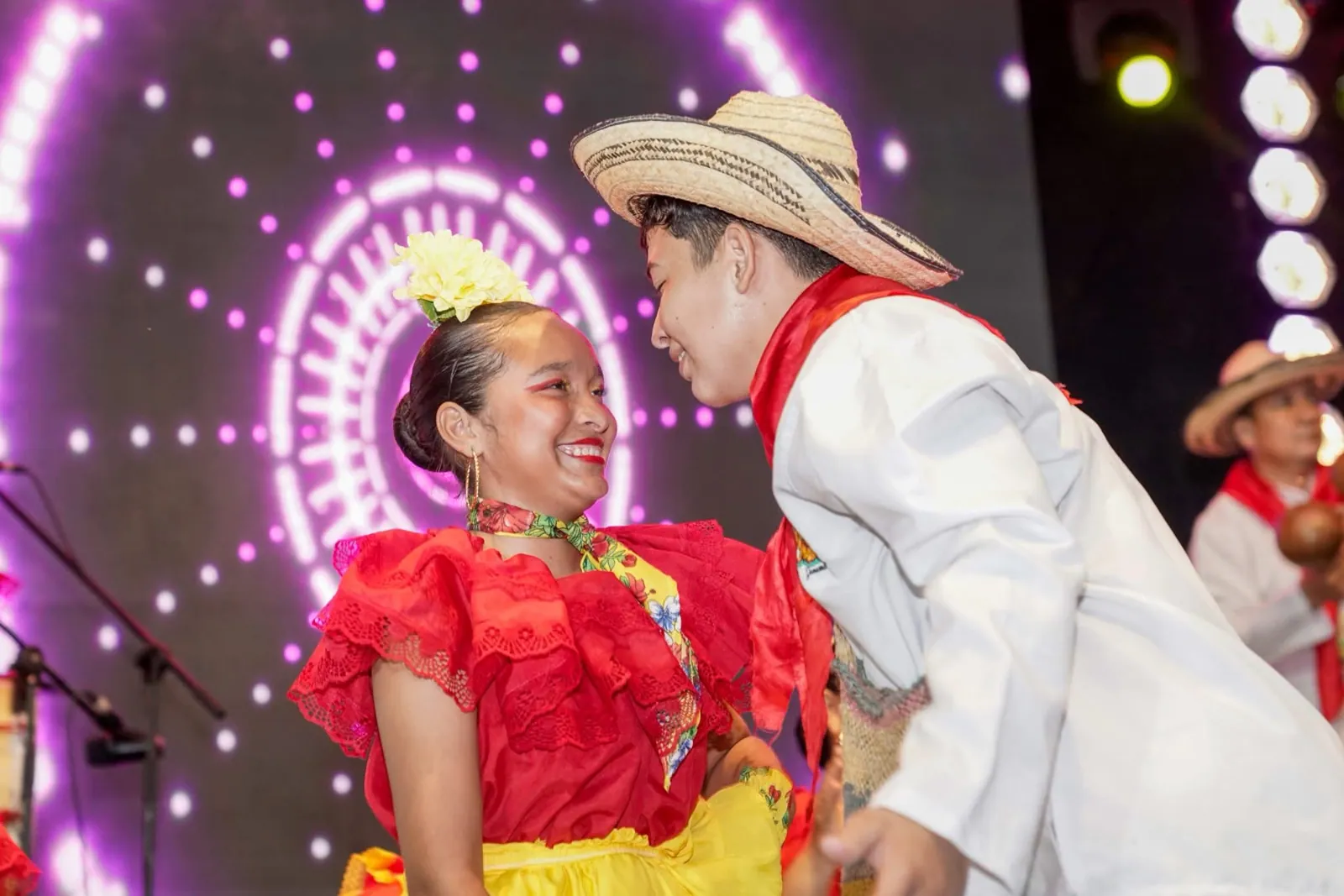 Pareja de bailadores con vestuario típico rojo y sombrero danza bajo las luces de una tarima.